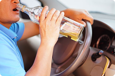 A man drinking alcohol from a bottle while driving - Leckerman Law, LLC