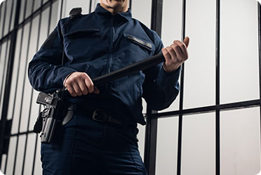 A uniformed man stands guard with a gun and stick in front of a jail cell - Leckerman Law, LLC