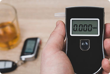 A person holding a breath alcohol tester near a glass of alcohol - Leckerman Law, LLC