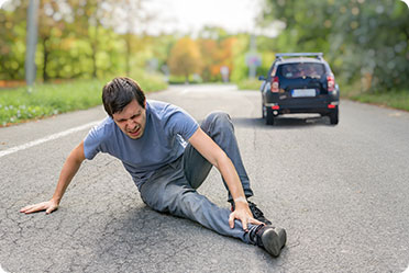 A man kneeling on the road with his injured leg - Leckerman Law, LLC