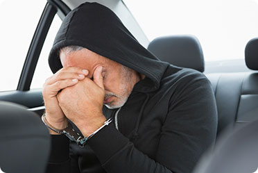 A person handcuffed sitting in the back seat of a car - Leckerman Law, LLC