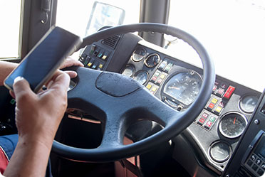 A person in the driver's seat of a bus using a cell phone - Leckerman Law, LLC
