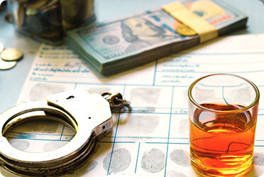 A glass of alcohol, handcuffs, and money on a table - Leckerman Law, LLC