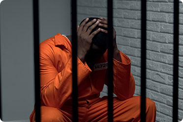 A man in orange prison clothes sits in a jail cell - Leckerman Law, LLC