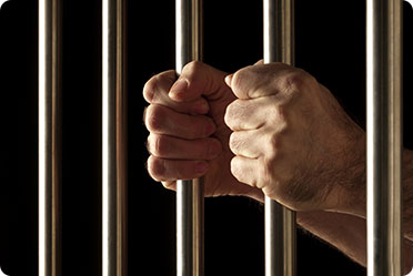 A man's hands are seen behind bars in a jail cell - Leckerman Law, LLC