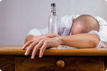 A man sleeping on a table with a bottle of alcohol nearby - Leckerman Law, LLC