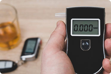 A person holding a breath alcohol tester near a glass of alcohol - Leckerman Law, LLC