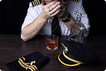 A uniformed man sits at a table, holding a glass of whiskey - Leckerman Law, LLC