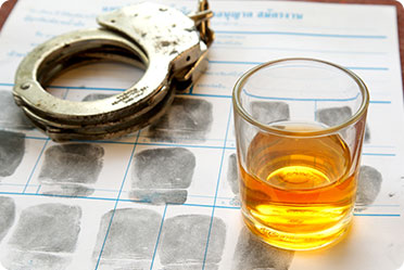 A table with a mug of alcohol and handcuffs placed on it - Leckerman Law, LLC